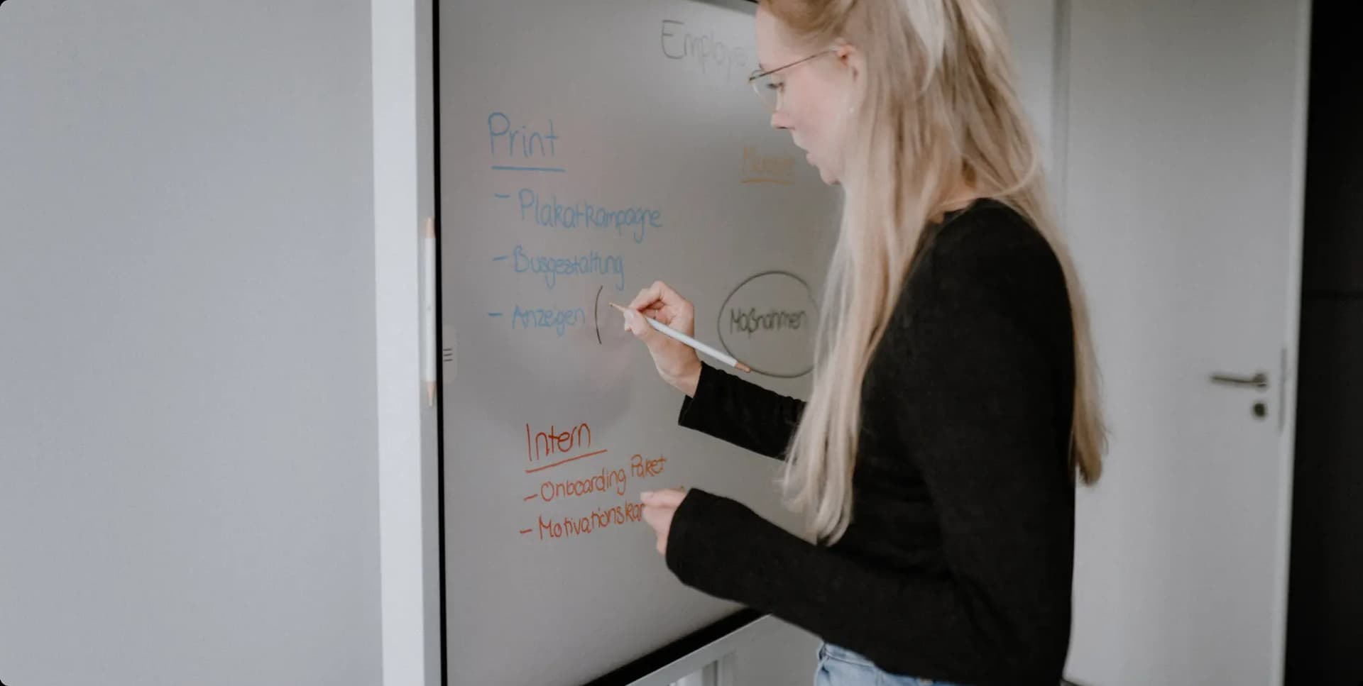 Frau schreibt mit Marker Ideen für Kommunikationskonzept an ein Whiteboard im Büro.