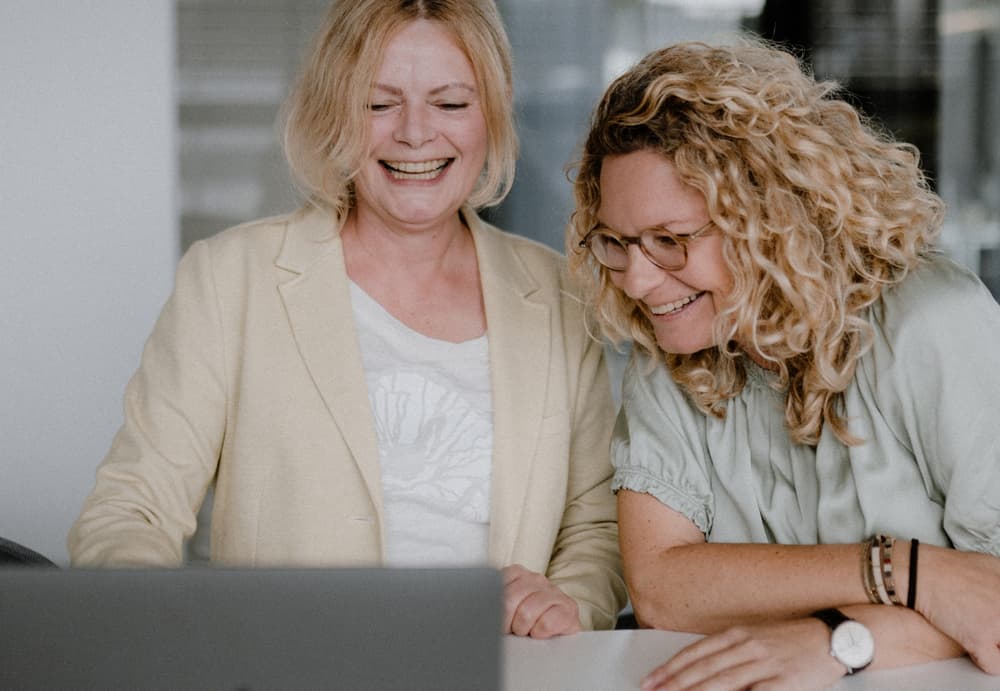Zwei lachende Frauen schauen auf einen Laptop.
