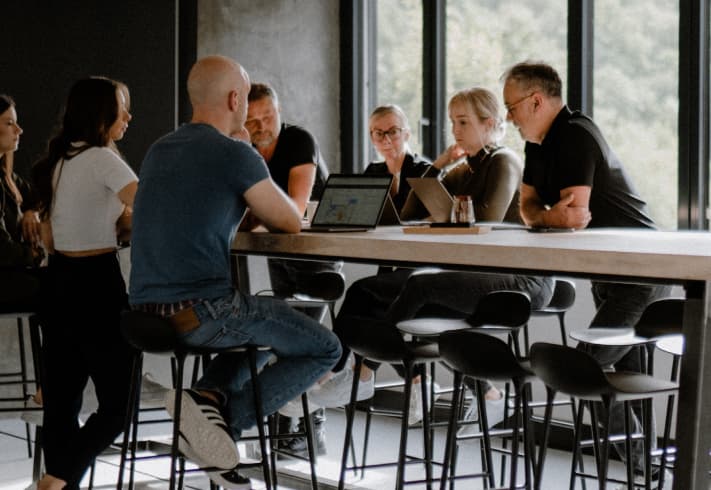 Mehrere Menschen der Digitalagentur reaze stehen an einem Hochtisch im Büro.